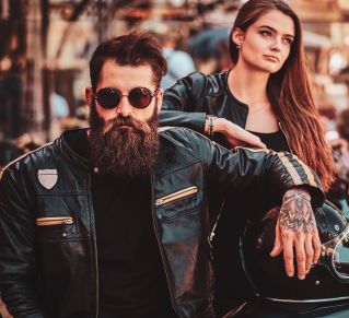 Good looking male biker with his tattooed hand resting on a helmet, and good looking woman behind him