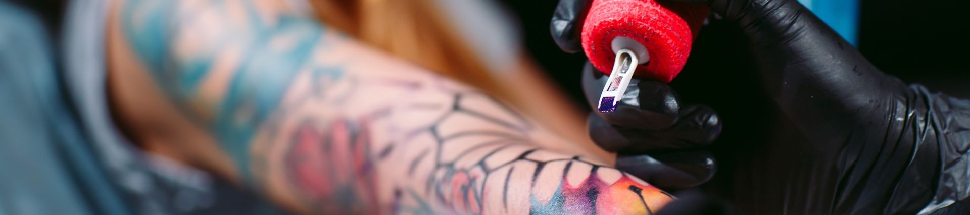 Close up of colorful sleeve tattoo in progress with the tattoo artist's gun resting a couple inches above