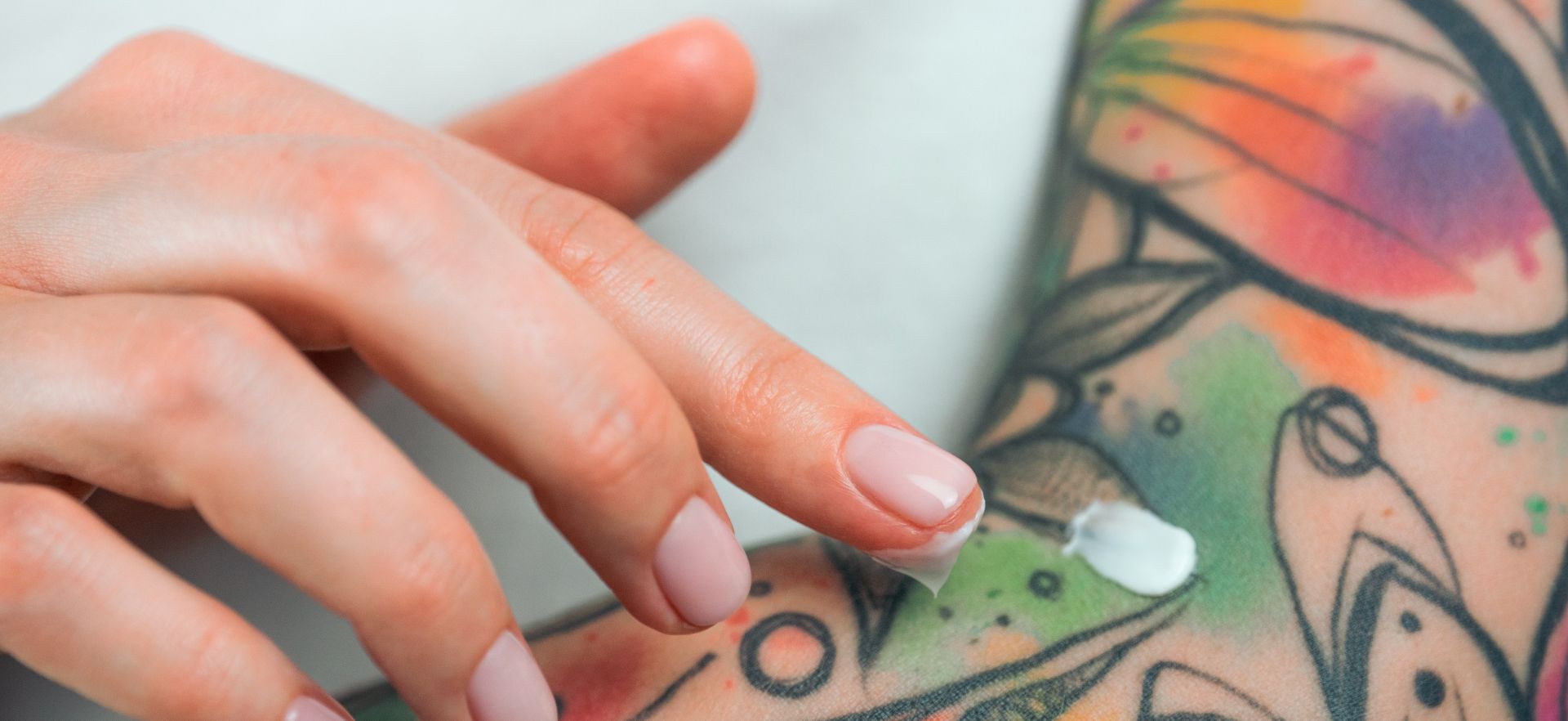 A tattooed left arm with the right hand spreading cream on the tattoo.