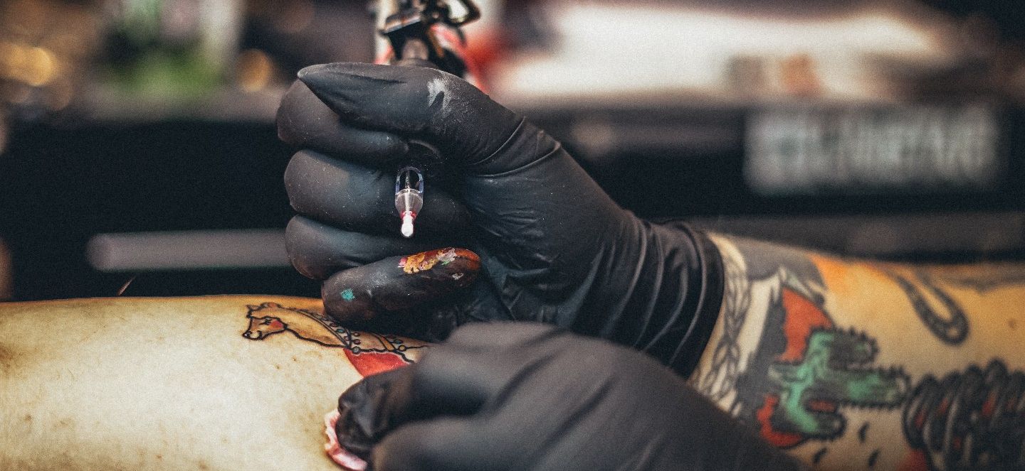 A tattooed right hand taking salve from a container to apply to a customer.